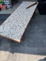 Full view of rectangular coffee table outdoors, showing mosaic tile top and detached leg resting on the table surface.