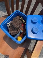 Blue LEGO plastic container with partially opened lid showing items inside on wooden chair outdoors