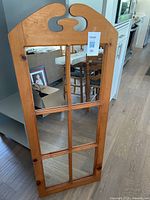 Full view of the solid wood framed hall mirror with eight glass panes and decorative top, standing on floor near kitchen area.