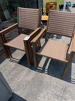 Two patio chairs side by side outdoors showing faux wood metal arms and woven wicker seats and backs.