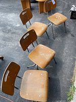 Four vintage wooden school chairs with metal legs arranged on asphalt showing wear and paint spots.