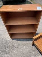 Front view of the wood and particle board shelf showing three open shelves and surface wear.