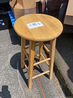 Full view of wooden stool showing round seat, four legs, and support bars in natural light.