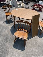 Photo of oval dining table with removable leaf standing upright, and three wooden chairs around it, showing the overall condition and setup.