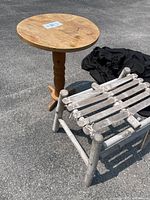 Photo showing round wood pedestal table and low whitewashed wooden stool with rope-tied slats, outdoor lighting.