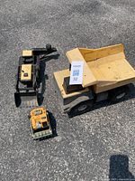 Three Tonka construction toys outdoors on asphalt: yellow dump truck, black excavator, small yellow bulldozer