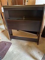 Front view of the dark wooden headboard with built-in drawers, showing scratches and wear.