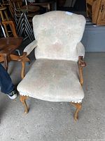 Front view of vintage upholstered armchair showing light beige patterned fabric and curved wooden legs and arms.
