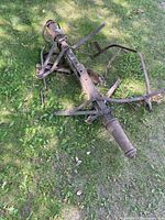 Old wagon axle lying on grass showing both metal and wooden sections with rust and weathering.