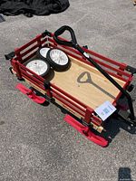 Red wooden wagon with red slatted sides and natural wood bottom bed, loaded with four plastic white and black wheels and black plastic ergonomic handle.