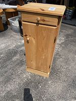 Front view of a small wood cabinet showing drawer and door with wooden knobs, standing on pavement outdoors.