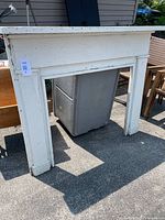 Front view of white antique wooden fireplace mantle standing outdoors, showing full frontal rectangular shape with weathered white paint and solid wood construction.