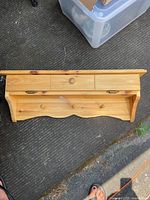 Top view of the wooden shelf with three wooden hooks and two small drawers, placed on a pavement surface.
