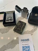 Three Zippo lighters and black leather case on white marble surface.