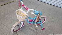 Side and angle view of 16 inch children's bicycle showing blue frame, training wheels, front basket, and handlebar streamers.