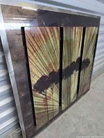 Close-up angled shot showing the abstract tree silhouettes and radiant rays on the metal wall art.