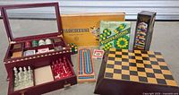 Photo showing all games including wooden chess set in box, Parcheesi box and board, cribbage board, Puzzlations box, Attack game box, and deck of playing cards.