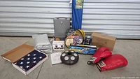 Wide photo showing all lot items including boxing gloves, car cover, American flag, jumper cables, lock box, spotlight box, umbrella light and traffic recorder figure.