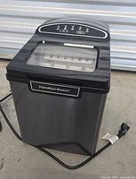 Full view of Hamilton Beach countertop ice maker showing stainless steel body, clear top lid, and power cord.