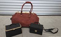 Set of three bags: large brown travel bag with two handles, and two black bags in front, a vanity case with top handle and rectangular organizer bag with shoulder strap.