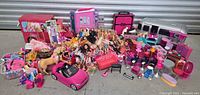 Wide shot showing over 70 dolls (Barbie, Monster High, Ever After High), various playsets including camper van, RV trailer, pink convertible car, and doll furniture in pink and purple tones.
