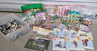 Wide view showing multiple LEGO items including boxed sets, bags of bricks, assembled house, and instruction manuals