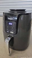 Front view of Ninja AF101 S5 air fryer powered on with control panel display showing timer and function buttons.