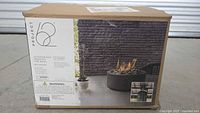 Box of Project 62 Outdoor Gas Tabletop Fire Bowl showing product details and an image of the fire bowl in use on a patio table.