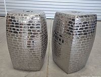 Pair of silver metallic finish ceramic garden tables with crocodile texture, standing on a concrete floor, shown in angled front view.