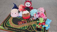 Top-down view of all 11 plush toys arranged on Melissa & Doug play mat showing variety in characters and colors.