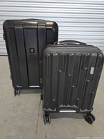 Two black hard-shell suitcases showing front views with brand logos, vertical and geometric molded design.