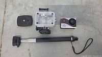 WiFi HD Sports Cam ONE action camera with all included accessories laid out: black mounting plate, waterproof case, action camera unit, telescoping selfie stick with wrist strap.