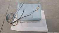 Front view of light blue leather crossbody bag with shoulder strap and original branded dust bag underneath.