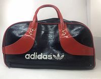 Front view showing Adidas Trefoil logo, navy vinyl body, red overlays and handles