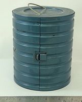 Closed ribbed blue metal cylindrical film canister with latch, ruler for scale