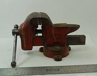Side view of red cast iron swivel bench vise fully closed with ruler for scale