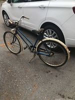 Photo of used vintage blue J.C. Higgins bicycle parked near cars, shows the left side profile with visible basket, saddle, and frame details.