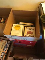 Top view of cardboard box filled with books including two visible Lawrence Sanders books titled 'The Passion of Molly T.' and its back cover.