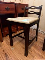 Side angle view of the vintage wood chair showing the vinyl seat and dark wood frame, set against wooden floor and some furniture in the background.