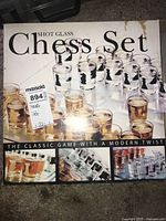 Box front showing the shot glass chess set with 32 shot glasses and a chessboard, both clear and amber colored.