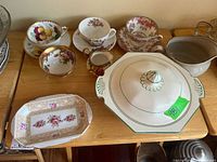 Wide view of collection of vintage teacups with saucers, Royal Albert floral tray, stoneware cream pitcher, Royal Winton covered bowl on wooden table.