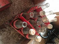 Twelve empty Coca-Cola glass bottles in two red cardboard carrying cases branded with Coca-Cola Classic, some with caps on, others open.