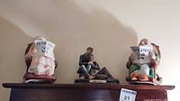 Photo showing two ceramic banks and Louis Dionne figurine on top of wooden furniture.