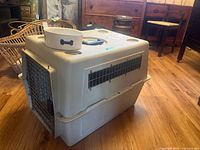 Side and top view of the beige plastic pet carrier with black metal wire door, bowl sitting on top.