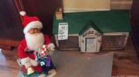 View of vintage Santa Claus figurine holding gifts next to the vintage metal doll house