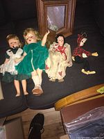 Four assorted vintage dolls placed on black surface showing full body and outfits