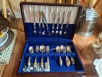 Full open case showing evenly spaced compartments holding 24 pieces of flatware including knives, forks, and spoons on blue velvet lining.