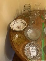 Photo shows assorted glass pitchers, beer mug, and bowls arranged on a wooden table.