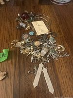 Assorted costume jewelry with earrings, charms, and pins on wooden surface.