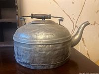 Front angled view of a metal hammered kettle on a flat surface showing handle and spout details.